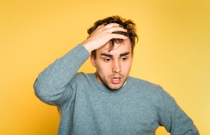 Worried adult man sitting on a sofa with hands clasped, contemplating whether to get tested for an STI.