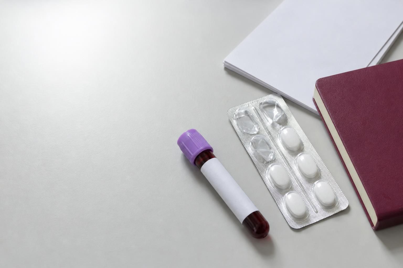 A lavender-top blood collection tube and a blister strip of plain white tablets on a clean lab bench, representing the two checkpoints of viral load testing and daily dosing.