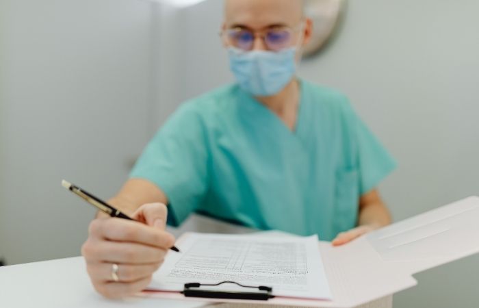 Clinician at a desk in a private consultation room, representing the link from at-home rapid test to confirmatory clinical care.